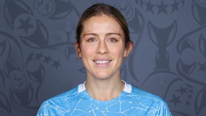 Abby Dahlkemper wears a blue soccer jersey and smiles for the camera.